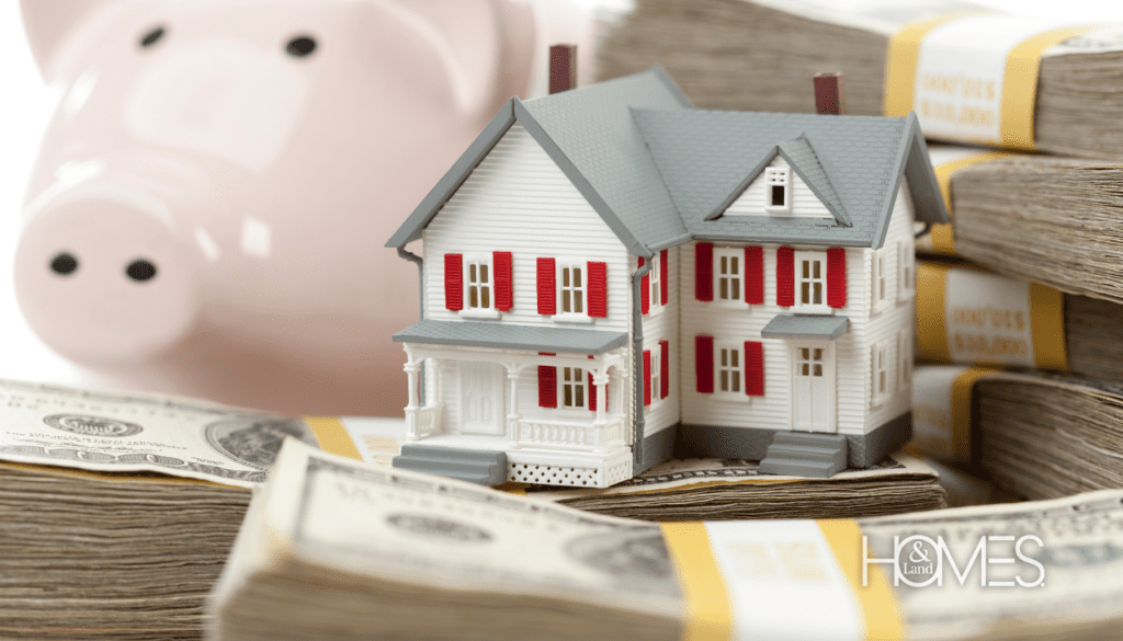 A piggy bank, miniature house, and a stack of $100 bills are stacked together, symbolizing the financial importance of setting a marketing budget for a real estate agency.